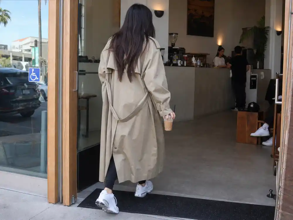 Trench coat leggings and white sneakers coffee run outfit illustrating how to dress like Hailey Bieber off duty morning routine
