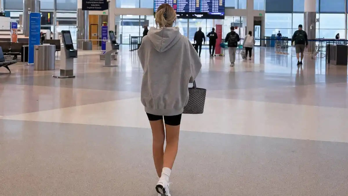 How to dress like Kendall Jenner airport style — oversized grey hoodie black biker shorts and white sneakers at airport terminal seen from behind