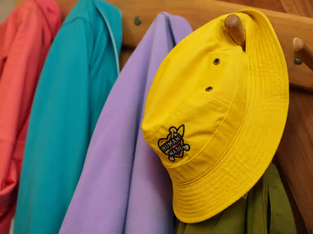 Bright yellow bucket hat on coat hook central to how to dress like Pharrell Williams colorful style headwear rotation