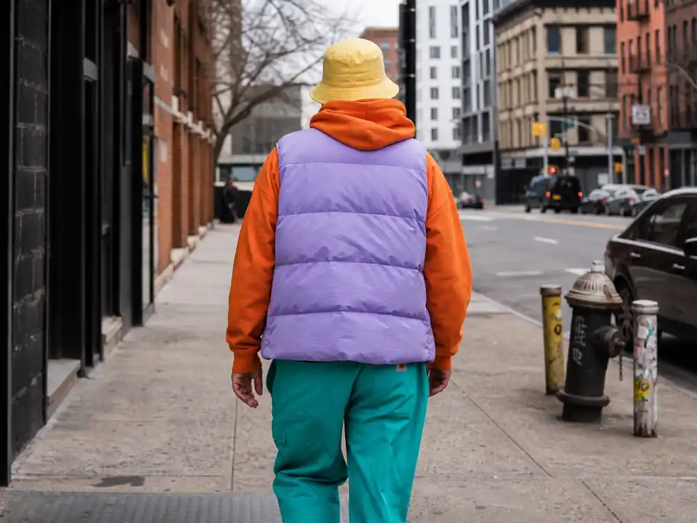Layered lavender puffer orange hoodie and teal pants behind how to dress like Pharrell Williams colorful style streetwear codes