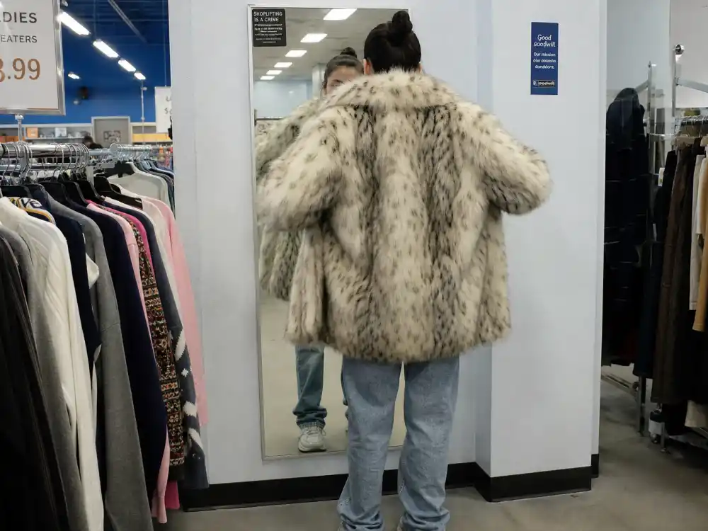 Trying oversized coat at thrift store mirror behind how to dress like Rihanna on a budget secondhand shopping
