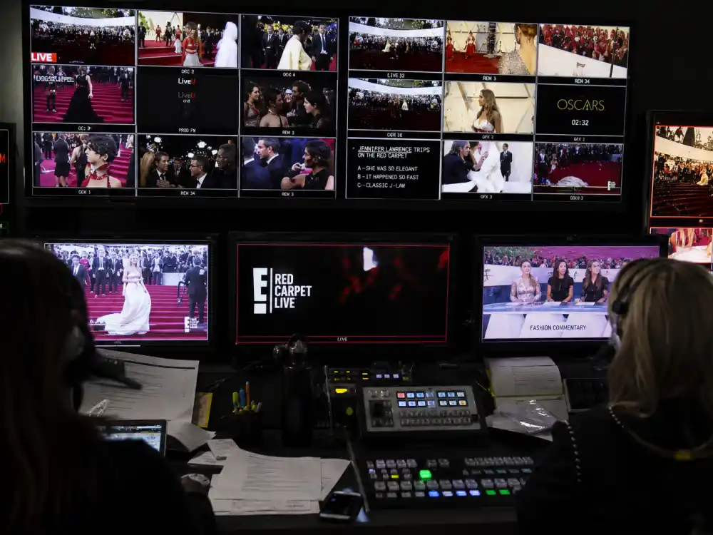 Television fashion commentary and media gallery monitors documenting Jennifer Lawrence tripping Oscars dress viral broadcast reaction worldwide