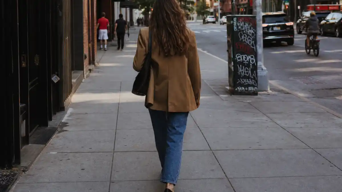 Kaia Gerber model off duty style — straight-leg jeans white tank oversized camel blazer and black loafers on NYC sidewalk seen from behind