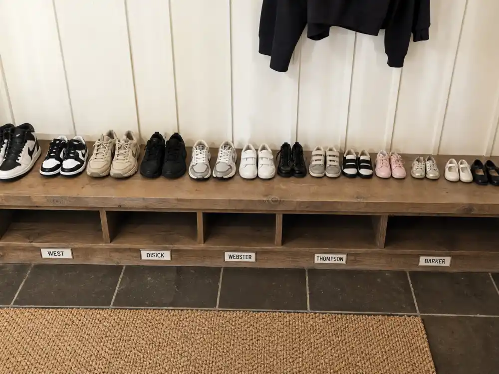 Thirteen cousin shoe pairs with surname tags for Kardashian Jenner kids blended family explained — teen sneakers through toddler sizes on mudroom bench