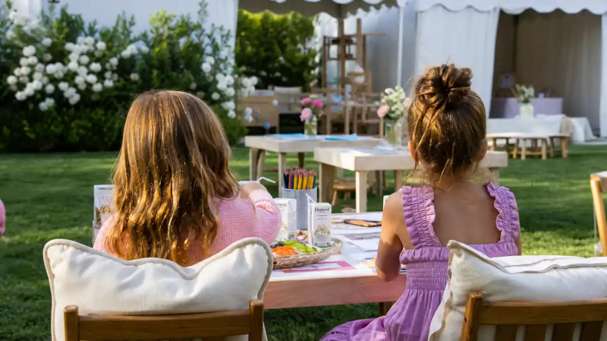 Kardashian Jenner kids godparents and friends — luxury backyard playdate setup from behind with craft table juice boxes and cousin gathering without faces