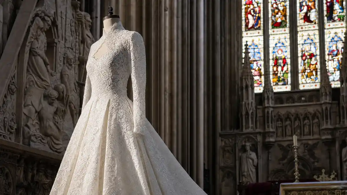 Kate Middleton wedding dress Alexander McQueen — ivory lace long-sleeve royal gown on mannequin in Westminster Abbey style cathedral with stained glass light