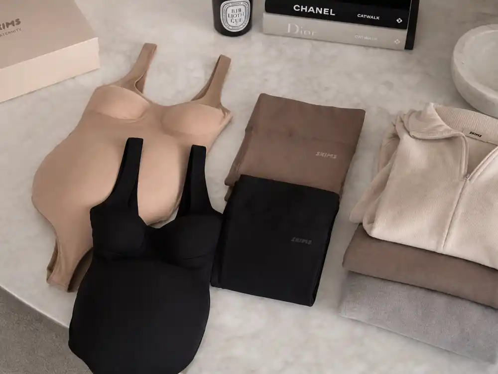 Neutral beige and black maternity shapewear bodysuits flat lay central to Kim Kardashian maternity street style Skims-era loungewear and body-conscious base layers