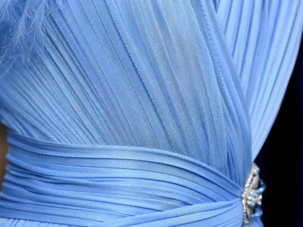 Accordion pleating technique defining the Lupita Nyongo blue Oscars gown — macro detail of powder sky-blue silk pleats catching flash photography