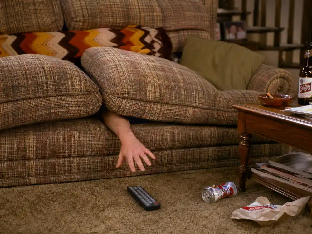 Hand reaching into battered couch cushions for remote evoking the Married with Children cast where are they now living room gag