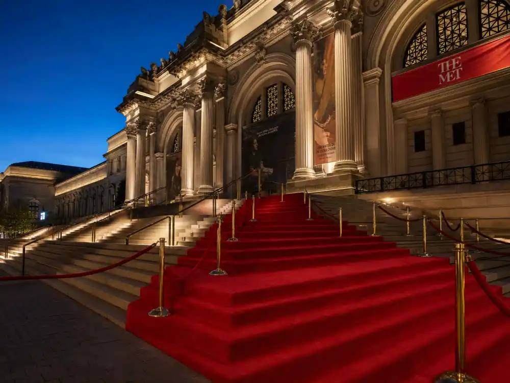 Metropolitan Museum grand staircase with red carpet runner and velvet rope stanchions ready for Met Gala best dressed all time arrivals at dusk