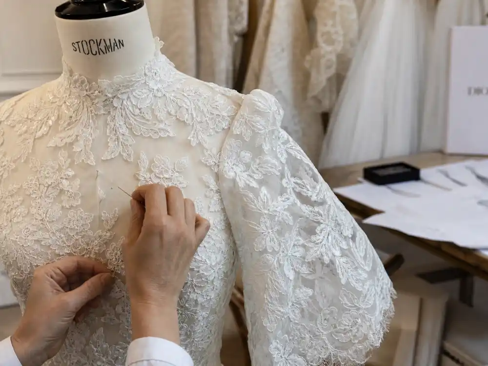Dior Paris atelier hands stitching ivory lace onto Miranda Kerr wedding dress Maria Grazia Chiuri high-neck bell-sleeve couture bodice on dress form