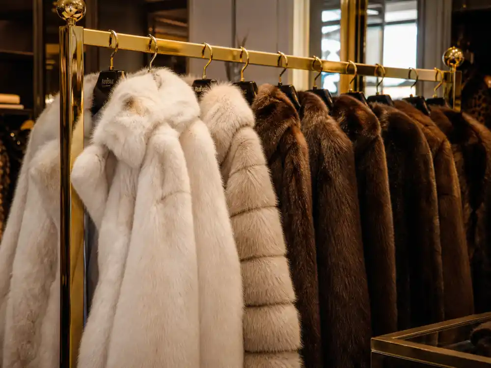 Faux fur coats in cream and brown on luxury boutique rack showing wardrobe foundation behind mob wife aesthetic celebrities red carpet and street rotations
