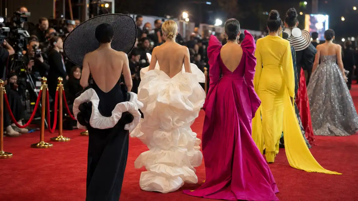 Most daring award show outfits ever — anonymous guests from behind in avant-garde evening gowns on a red carpet with paparazzi camera flashes