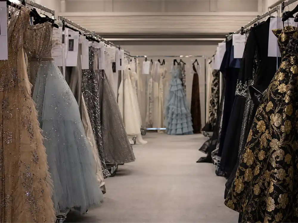 Haute couture evening gowns on rolling racks in designer showroom aisle showing luxury construction behind most iconic Met Gala looks ever atelier preparation