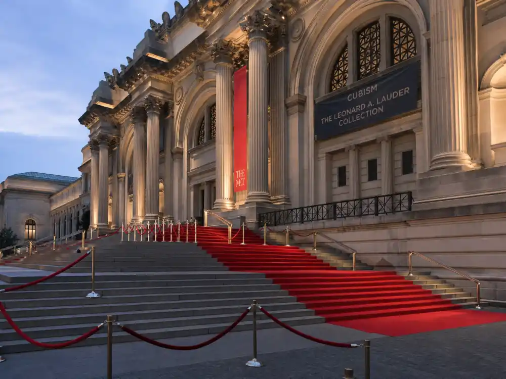 Metropolitan Museum grand staircase with red carpet runner and velvet rope stanchions ready for most iconic Met Gala looks ever arrivals at dusk