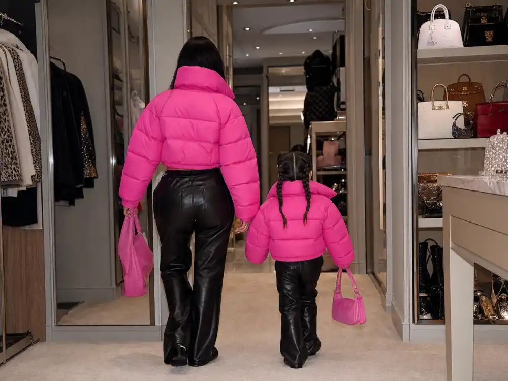 Matching hot pink puffer jackets on parent and child silhouettes from behind for most identical celebrity parent child pairs Kardashian Jenner Stormi Kylie lane