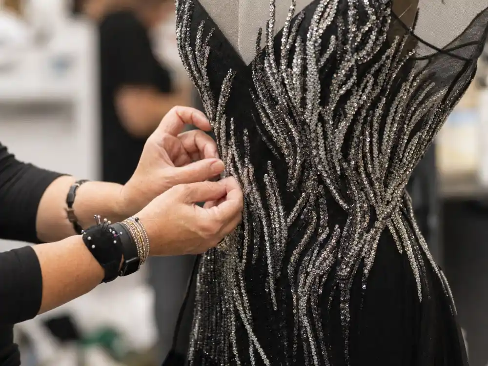 Stylist hands adjusting silver sequin beading on black Oscar evening gown bodice showing couture construction behind Oscars celebrity fashion 2026 atelier craftsmanship