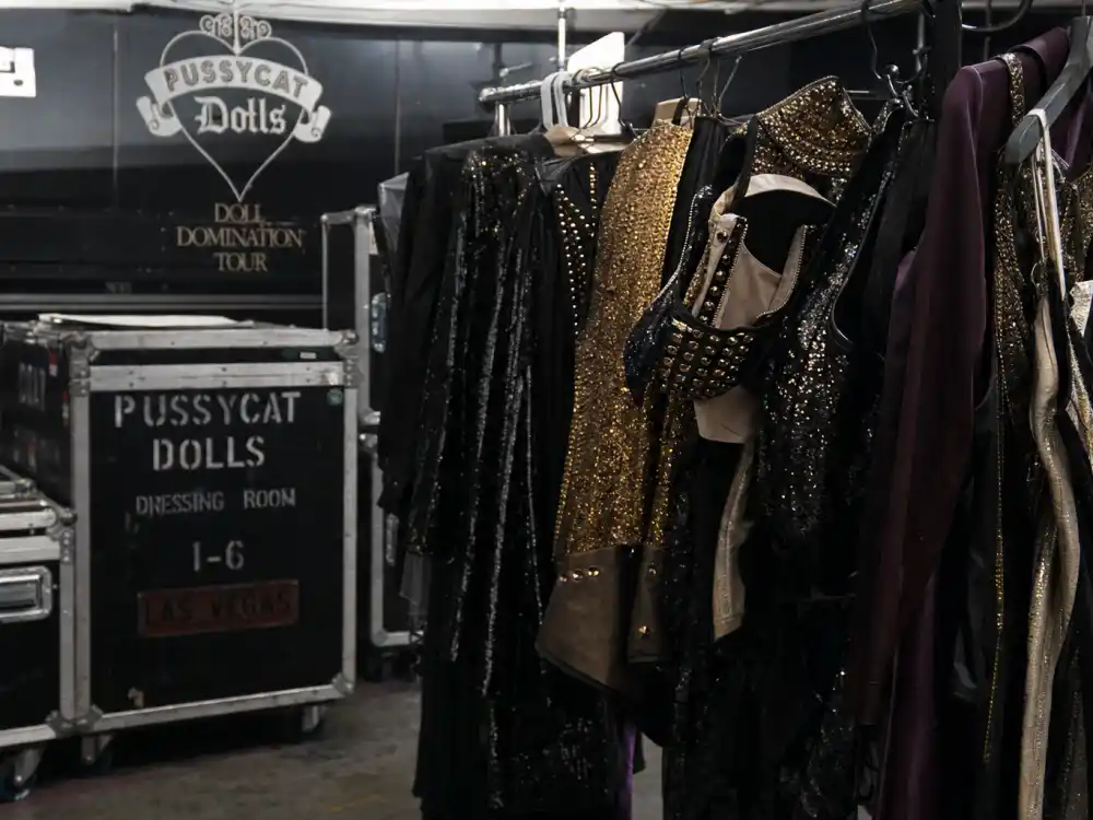 Concert tour backstage wardrobe racks evoking the Pussycat Dolls reunion tour era that never fully stabilized
