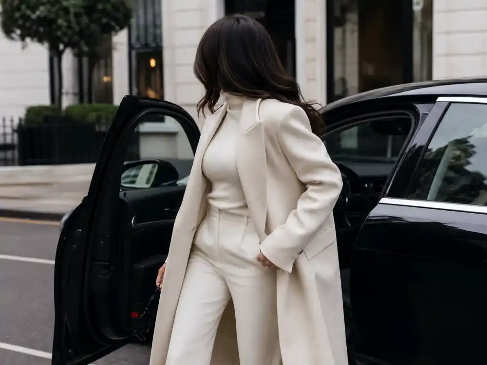 Anonymous woman from behind exiting car in quiet luxury celebrity style ivory turtleneck and tailored coat for paparazzi-ready understated street dressing