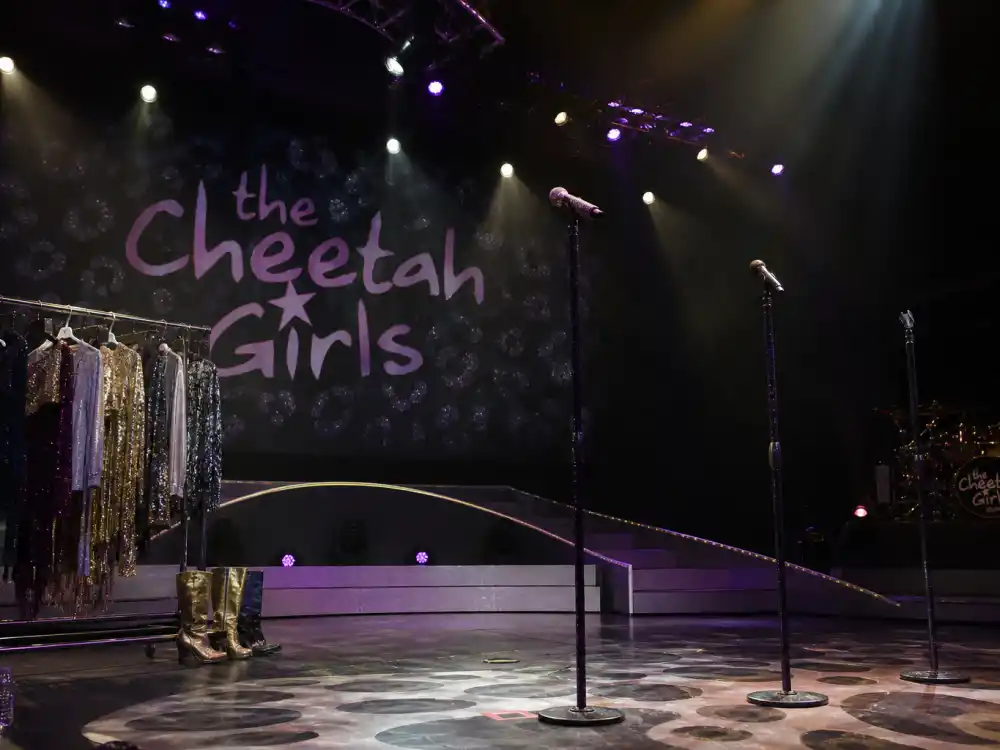 An empty pop girl-group stage with sequined costumes representing Raven-Symoné and The Cheetah Girls music career