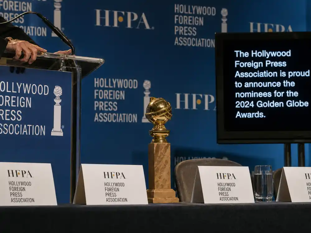 HFPA press table beside teleprompter illustrates institutional targets in Ricky Gervais Golden Globes monologues explained and HFPA backlash cycles