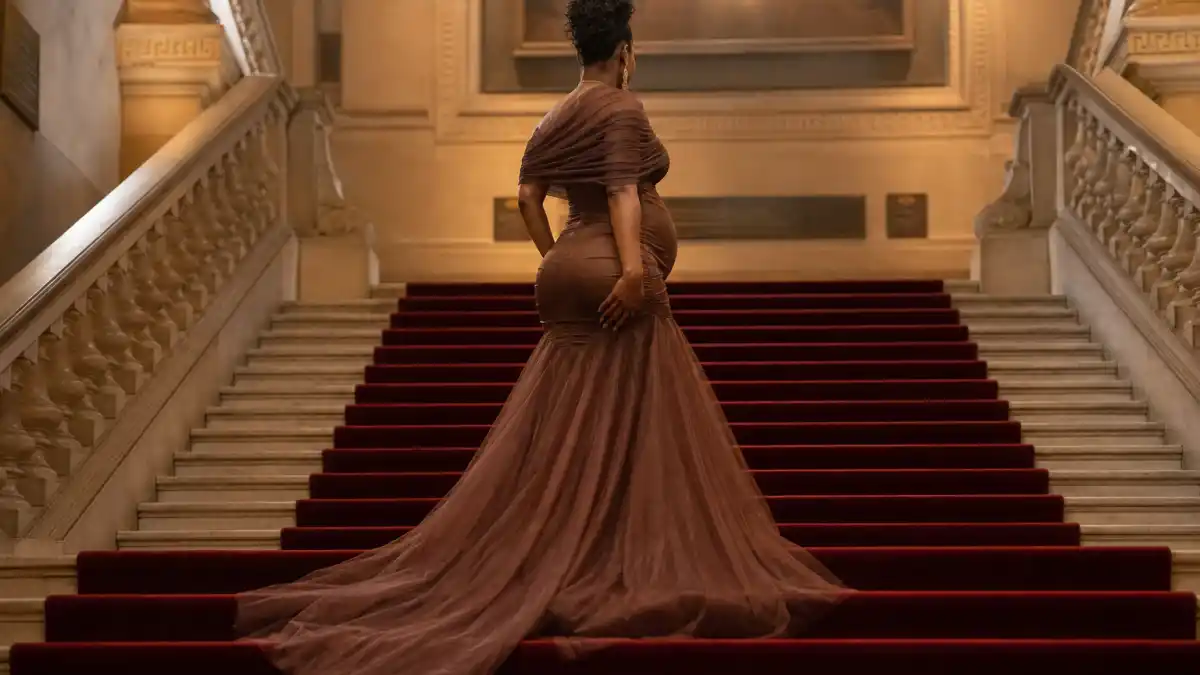 Rihanna pregnancy style evolution — anonymous woman in sculptural white Valentino-style maternity gown on Met Gala red carpet stairs seen from behind with visible baby bump