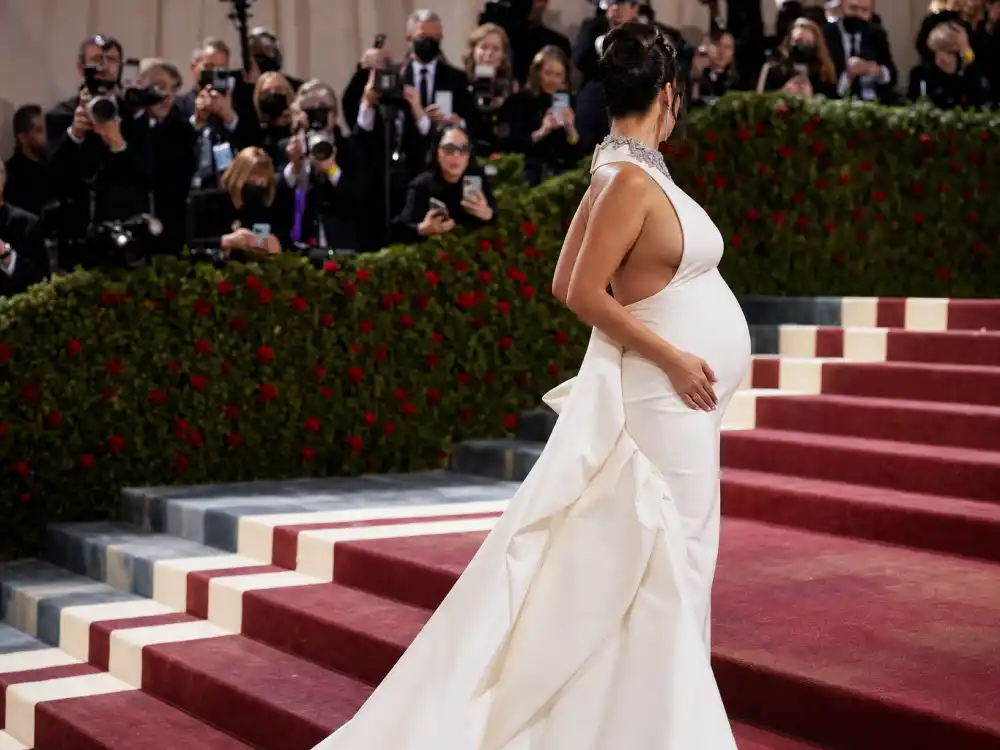 Anonymous pregnant woman in white sculptural gown on museum grand staircase for Rihanna pregnancy style evolution Met Gala 2023 maternity moment
