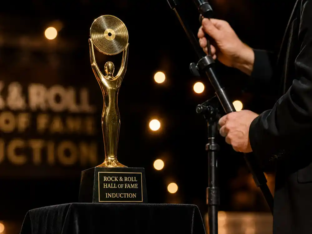 Golden Rock and Roll Hall of Fame 2026 inductees trophy on velvet pedestal beside induction ceremony microphone podium