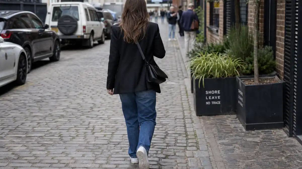 Sophie Turner off duty fashion — black oversized blazer straight-leg jeans white sneakers and crossbody bag on London cobblestone seen from behind