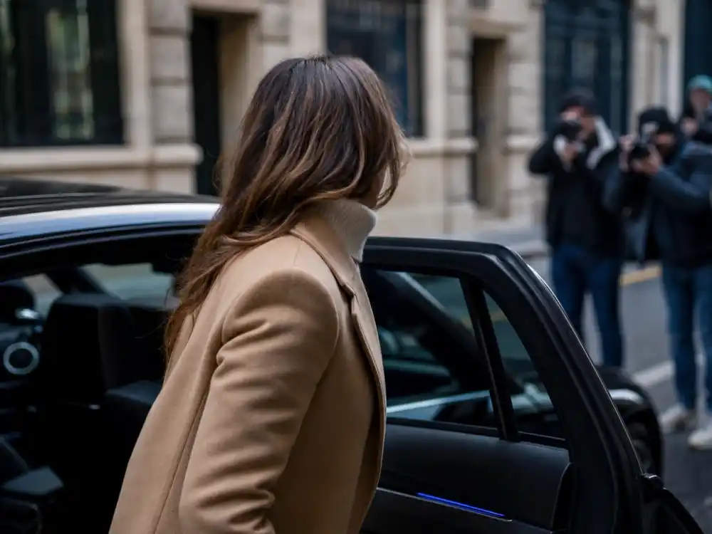 Anonymous woman from behind exiting car in stealth wealth celebrity fashion ivory turtleneck and tailored camel coat for paparazzi-ready understated street dressing