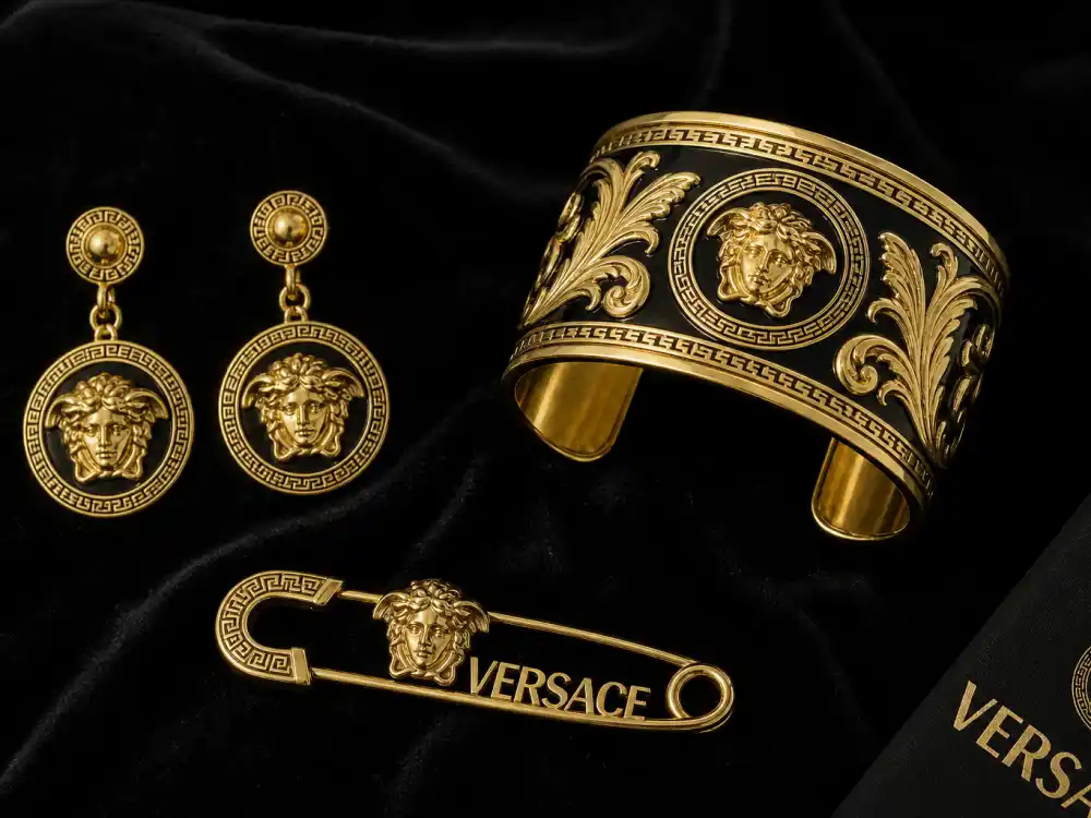 Gold Medusa earrings baroque cuff and safety pin brooch flat lay capturing accessory stacking rules stylists use when building Versace celebrity red carpet moments on camera