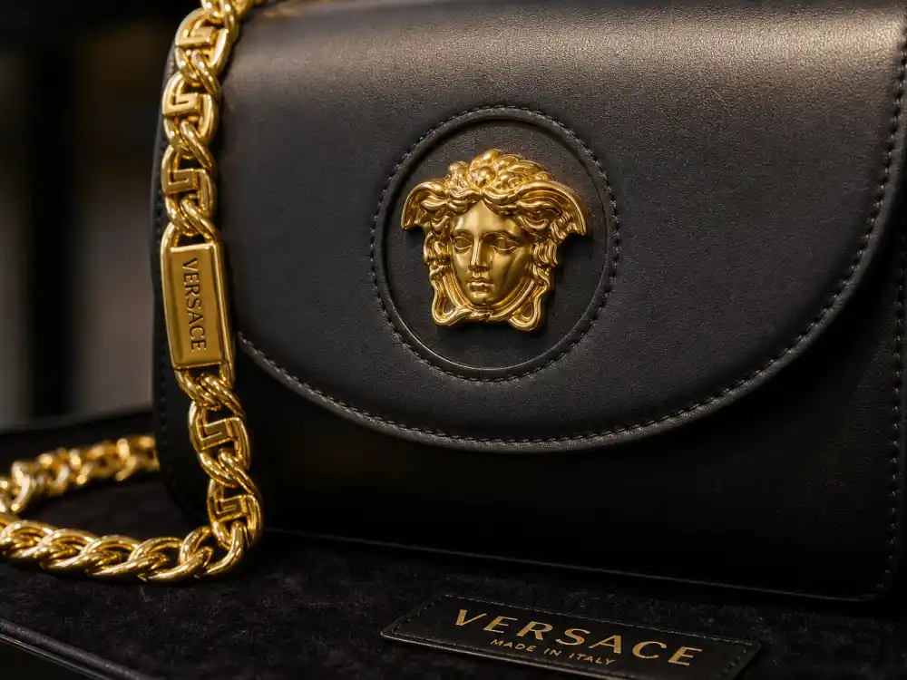 Gold Medusa head logo on black Versace handbag with baroque chain strap defining accessory codes behind iconic Versace celebrity red carpet moments at premieres