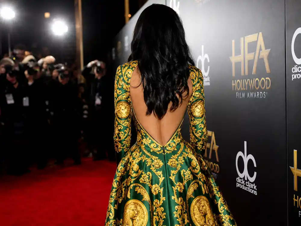 Anonymous woman in bold Versace baroque print gown photographed from behind at step-and-repeat showing how Versace celebrity red carpet moments command flash photography visibility
