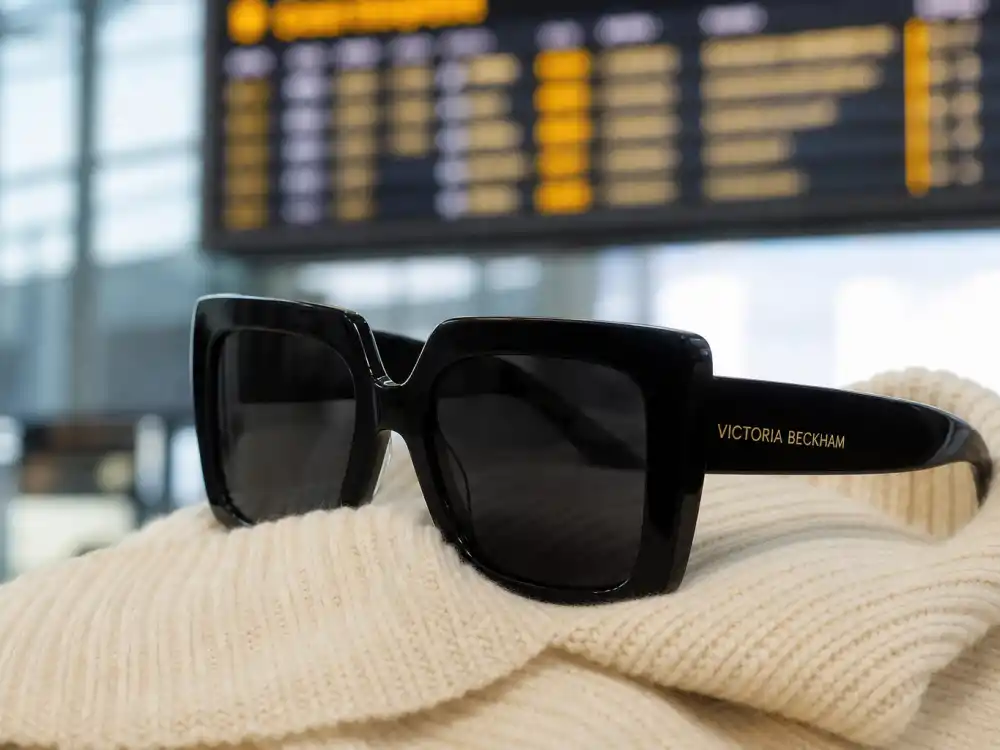 Oversized black square sunglasses on cream knit defining Victoria Beckham airport fashion face-framing accessory codes