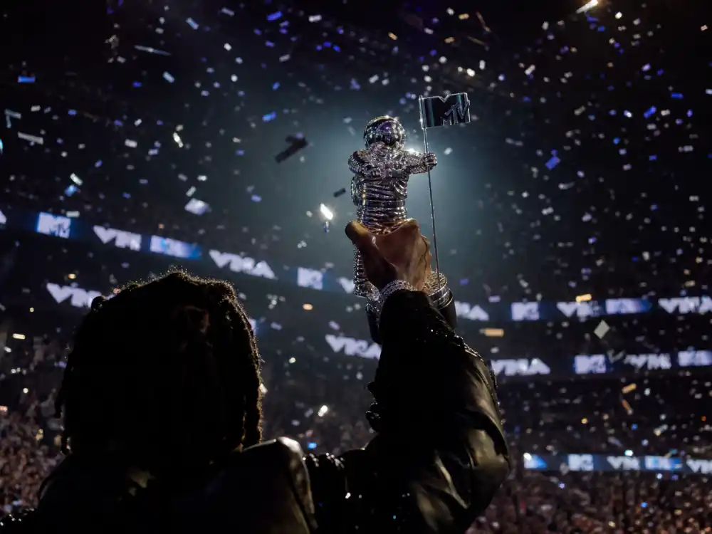 Famous VMA Moon Person trophy history moment — anonymous artist hands holding silver astronaut statuette on stage with confetti falling