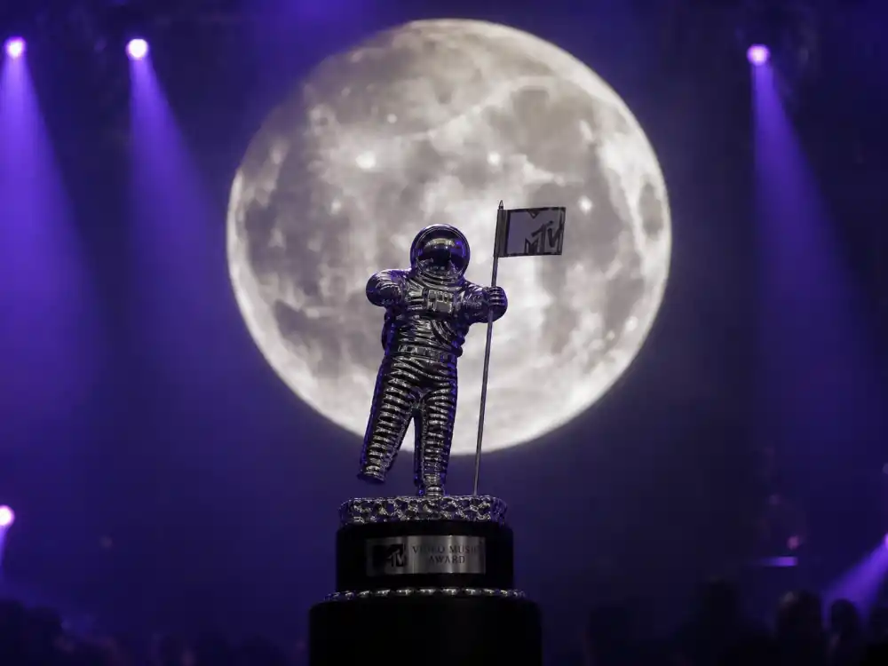 VMA Moon Person trophy history symbolism — silver astronaut statuette silhouette against full moon backdrop on MTV awards stage