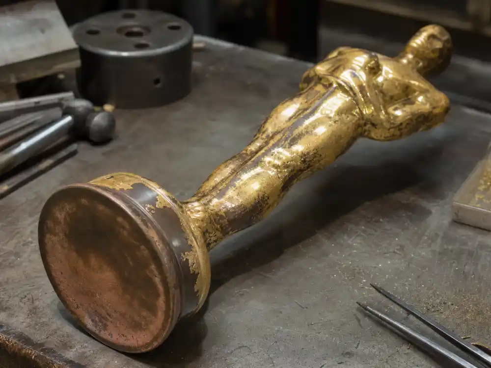 Oscar-style gold statuette on workbench showing bronze base metal beneath gold plating for what are award trophies made of and worth explainer