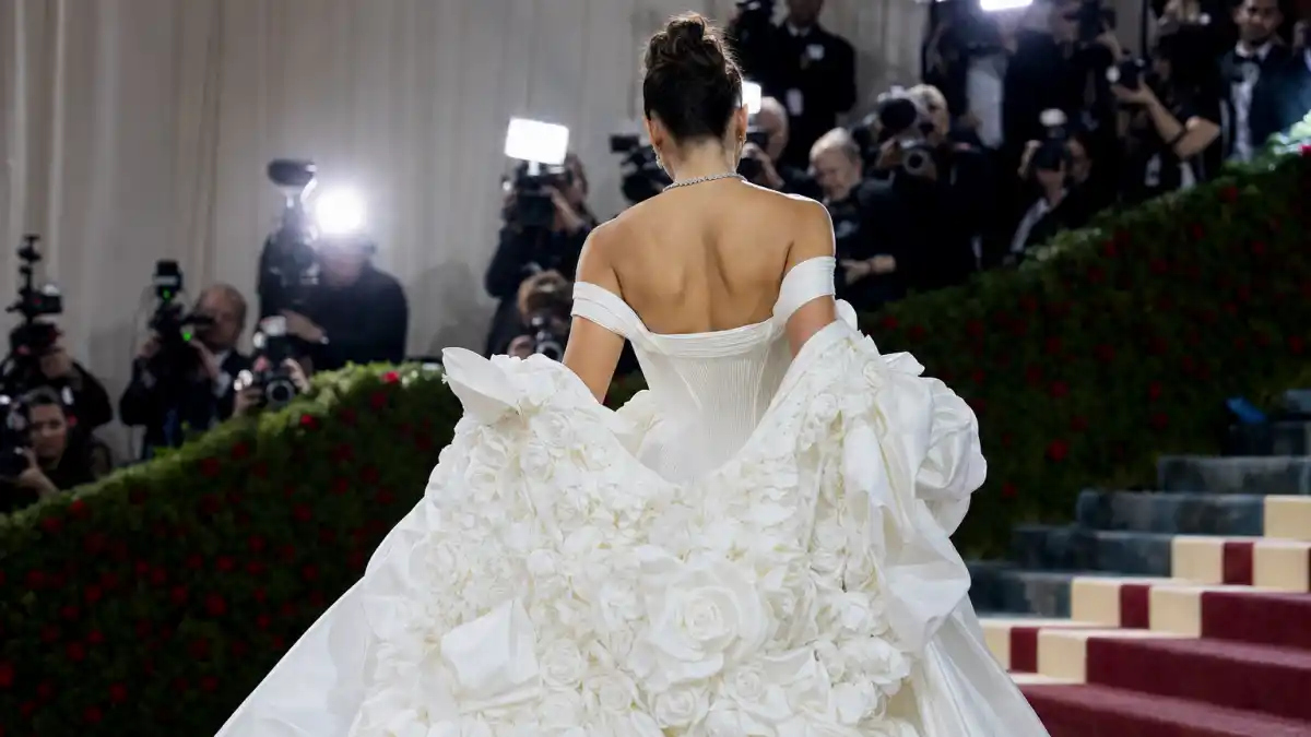 What did Gigi Hadid wear to Met Gala — white Thom Browne corset gown with yellow rose coat on museum steps seen from behind with camera flashes