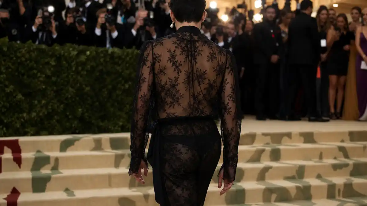 What did Harry Styles wear to Met Gala — sheer black lace Gucci gender-fluid outfit on museum steps seen from behind with pearl earring and camera flashes