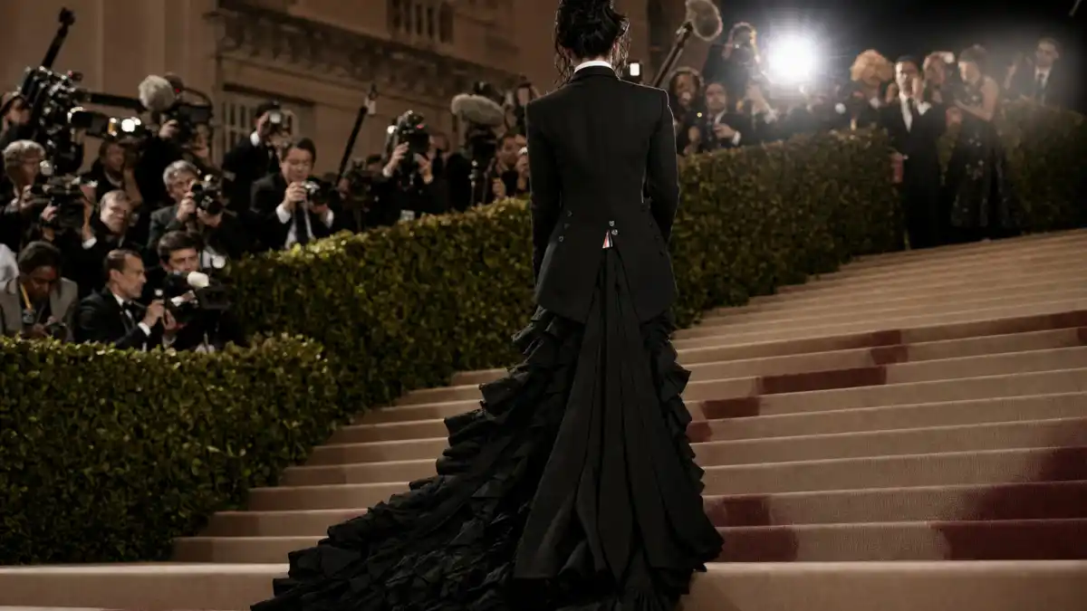 What did Jenna Ortega wear to Met Gala — gothic Thom Browne tailoring with long ruffled train on museum steps seen from behind with camera flashes