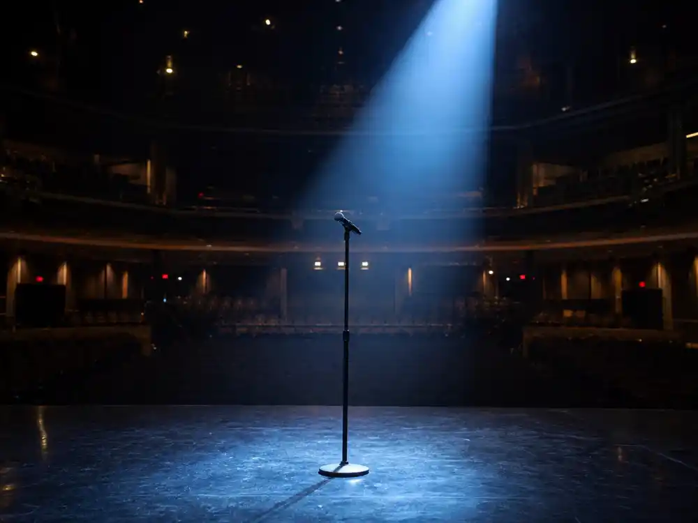 Empty theater stage microphone for what happened to Carlos Mencia now and his 2026 stand-up chapter