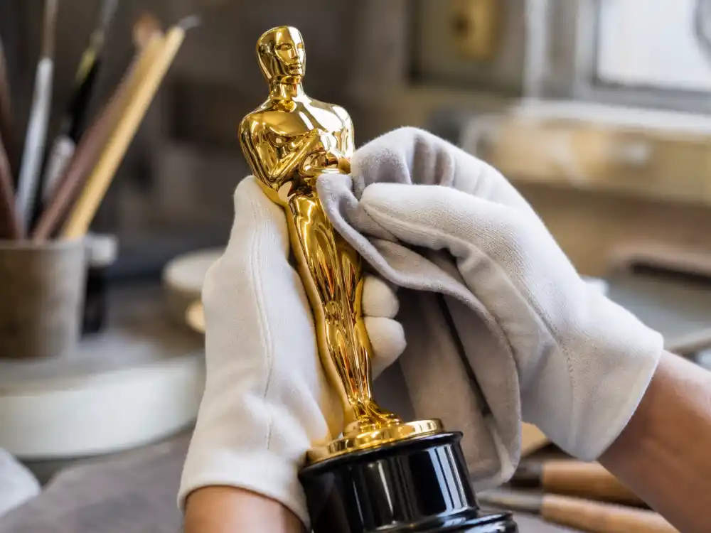 Gloved hands polishing a generic golden statuette — final finishing step in what is an Oscar statue made of today