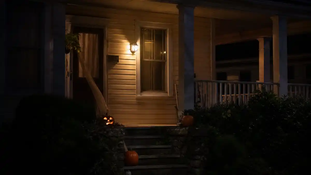 Where is Neve Campbell now 2026 — suburban porch at night with Halloween jack-o-lantern evoking Scream Sidney Prescott horror era