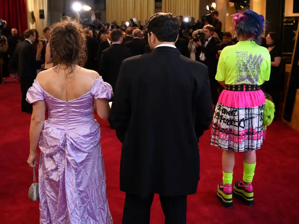 Worst dressed celebrities at award shows ever — three anonymous guests from behind in mismatched formal wear on major awards red carpet under camera flashes