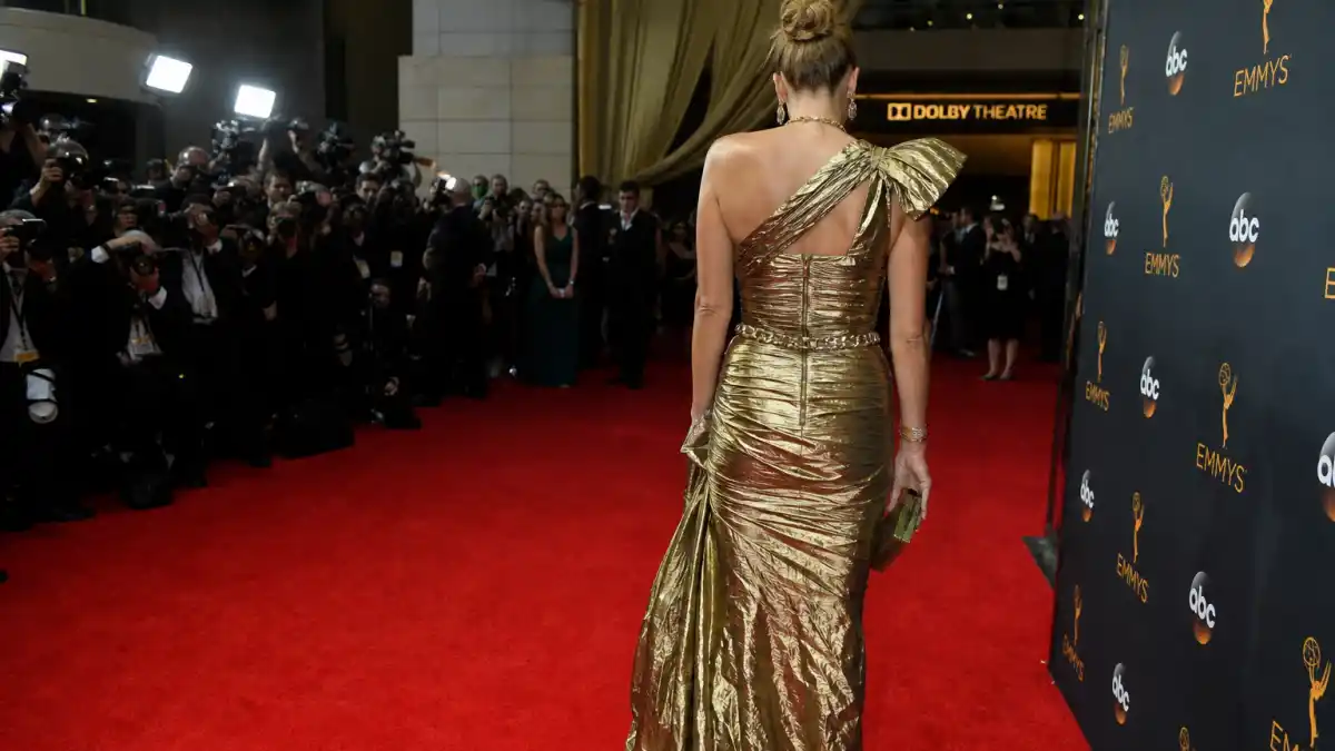 Worst dressed celebrities at award shows ever — anonymous guest from behind in crinkled metallic gold gown on Emmys-style red carpet with step-and-repeat backdrop