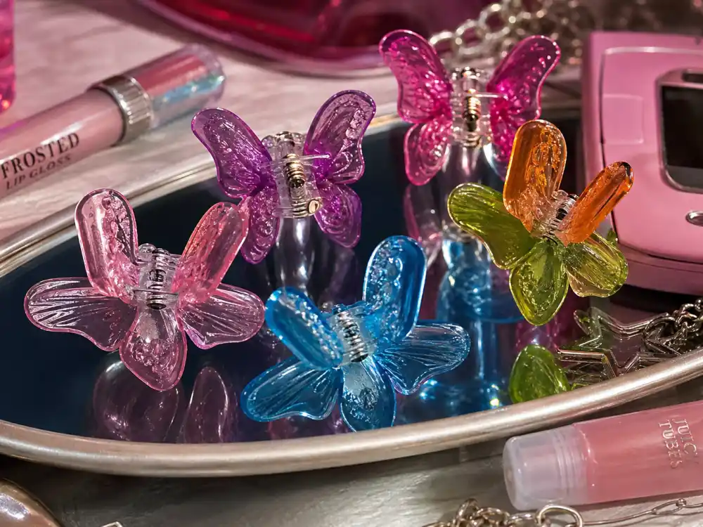 Colorful butterfly hair clips on vanity mirror with frosted lip gloss showing Y2K celebrity fashion trend beauty and accessory codes