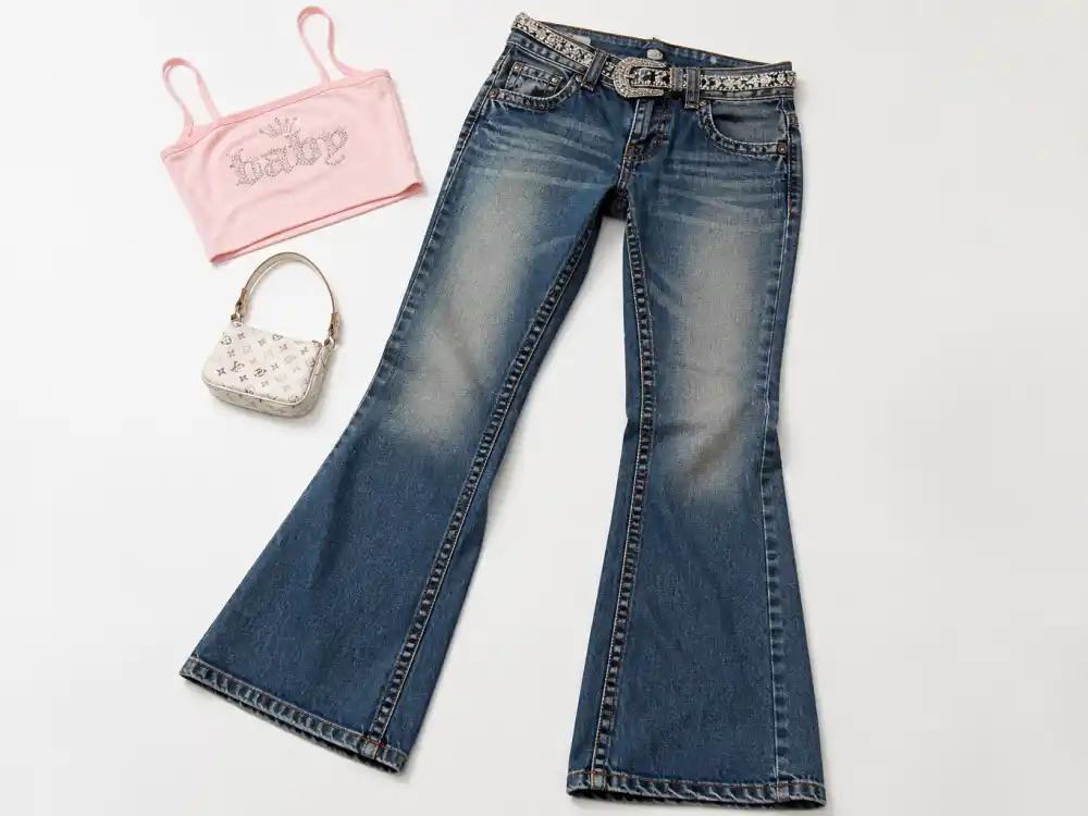 Low-rise flared denim jeans with rhinestone belt and tiny crop top flat lay defining the Y2K celebrity fashion trend denim silhouette