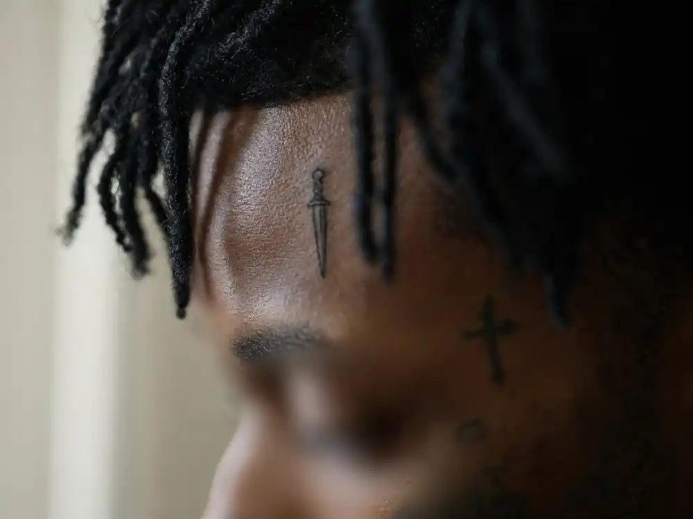 21 Savage tattoos and their meanings — close-up of signature forehead dagger knife tattoo between brows on Atlanta rapper side profile