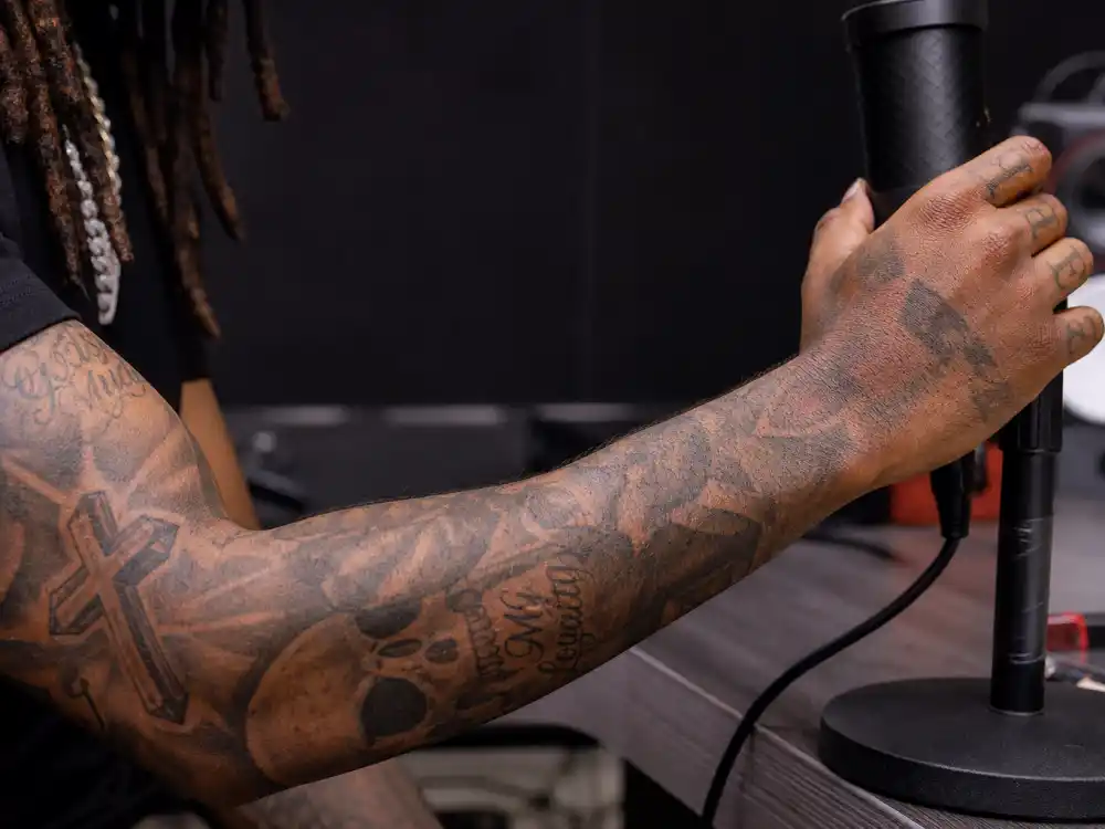 21 Savage tattoos and their meanings — heavily tattooed forearm sleeve with cross skull and script motifs on rapper arm at studio