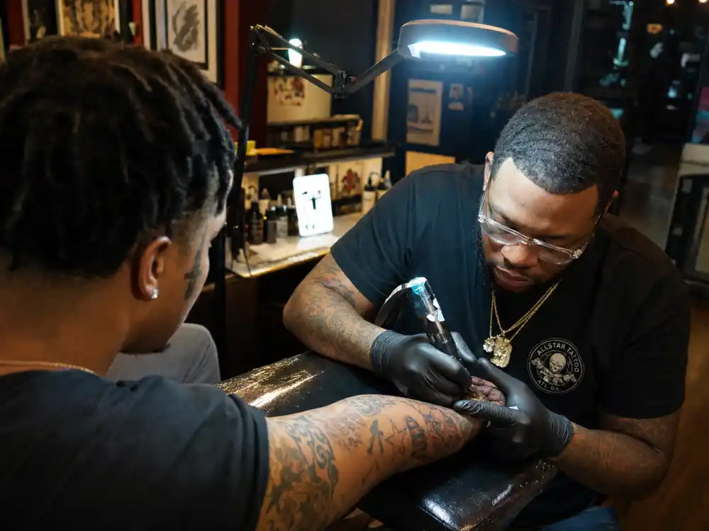 21 Savage tattoos and their meanings — tattoo artist working on client forearm sleeve in professional Atlanta studio session